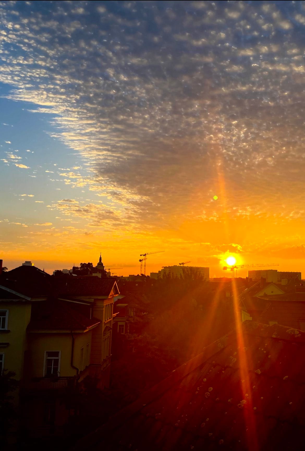 Die Sonne geht auf über den Dächern der Stadt, der Himmel ist voll mit kleinen Wölkchen, links sieht man das blau durchschimmern. (C) Herr Montag.
